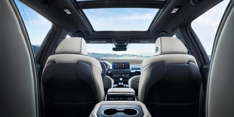 Interior view of a modern 2025 Acura MDX SUV showing two front seats, sunroof, and dashboard display.
