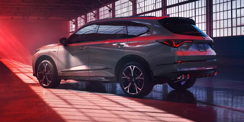 A 2026 Acura MDX Advance Package SUV is displayed inside a modern industrial space with dramatic red lighting, showcasing its sporty rear design, premium styling, and sleek LED taillights in Grapevine, TX.
